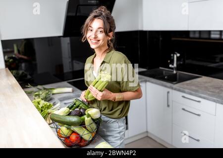 Porträt einer jungen und fröhlichen Frau mit gesundem Rohkost in der Küche zu Hause. Vegetarismus, Wohlbefinden und gesundes Lifestyle-Konzept Stockfoto