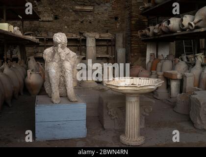 Gipsabguss von menschlicher Figur, mit Händen umklammert und Körper in einer Fötus-Position, sitzt neben einem Münze gefüllten Vogelbad, amphoras, Altäre, kleine Säulen, und Stockfoto