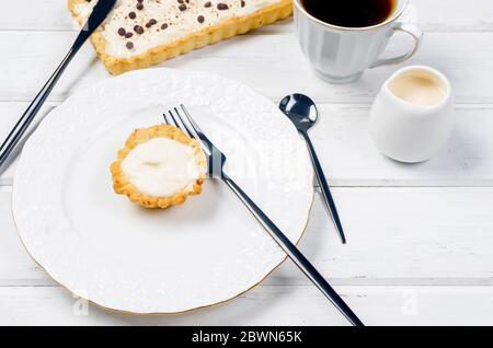 Tart mit Vanillecreme oder Käsekuchen mit Schokoladentropfen und Tasse Kaffee auf weißem Holztisch, Kopierraum, Draufsicht Stockfoto