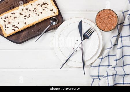 Tart mit Vanillecreme oder Käsekuchen mit Schokoladentropfen und Tasse Kaffee auf weißem Holztisch, Kopierraum, Draufsicht Stockfoto