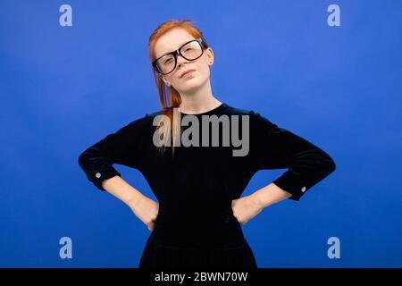 Ernst rothaarige Teenager-Mädchen mit ausgebreiteten Armen auf einem blauen Hintergrund mit Kopieplatz Stockfoto