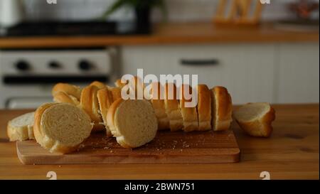 Nahaufnahme von geschnittenem Baguette auf Schneidebrett in der Küche. Gehacktes Weißbrot auf Holzbrett auf Küchentisch. Stockfoto