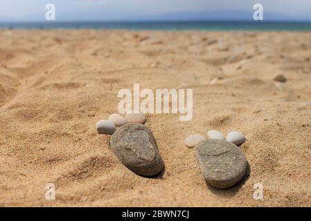 Fußabdrücke aus Kieselsteinen auf goldenem Strandsand Stockfoto