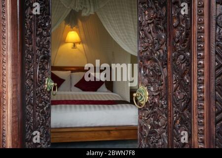 Traditionelles balinesisches Bett mit Baldachin. Blick durch die Öffnung der geschnitzten Türen. Stockfoto