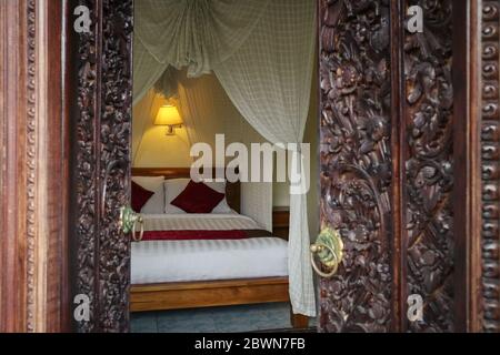 Traditionelles balinesisches Bett mit Baldachin. Blick durch die Öffnung der geschnitzten Türen. Stockfoto