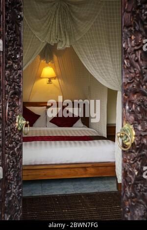 Traditionelles balinesisches Bett mit Baldachin. Blick durch die Öffnung der geschnitzten Türen. Stockfoto