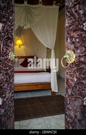 Traditionelles balinesisches Bett mit Baldachin. Blick durch die Öffnung der geschnitzten Türen. Stockfoto