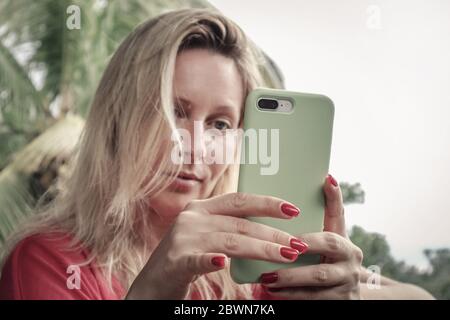 Erwachsene blonde Frau hält , mit und Blick auf Smartphone im Freien auf Bali Insel, Indonesien. Stockfoto