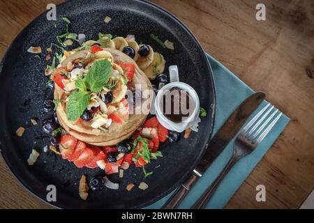 Pfannkuchen mit Banane, Heidelbeeren, Erdbeeren und Schokoladensauce auf einem Teller Draufsicht Stockfoto