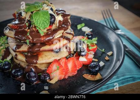 Pfannkuchen mit Banane, Heidelbeeren, Erdbeeren und Schokoladensauce auf einem Teller Nahaufnahme Stockfoto