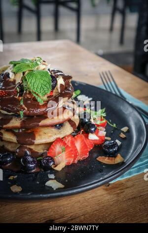 Pfannkuchen mit Banane, Heidelbeeren, Erdbeeren und Schokoladensauce auf einem Teller Nahaufnahme Stockfoto