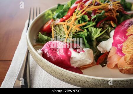 Geräucherter Lachs, Haschbraunkartoffel, halbgetrocknete Kirschtomate, Rübensoße, pochierte Eier, auf warmen Buttercroissant, Schnittlauch, gemischte Kräuter, Pistake zerdrücken Stockfoto