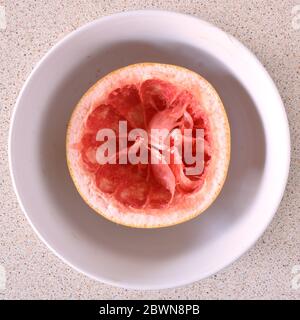 Luftaufnahme von oben nach unten und gefressene Grapefruit in einer weißen Schüssel auf einem hellen Hintergrund Stockfoto