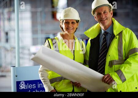 Porträt von zwei reifen Architekten in Schutzkleidung auf der Baustelle Blick auf Kamera hält eine Blaupause Stockfoto