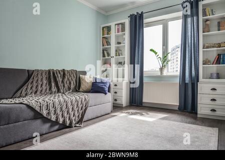 Helles, gemütliches Teenagerzimmer mit weißen Bücherregale, grauem Sofa und blauen Wänden Stockfoto