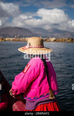 Die Frau aus der Uros-Gemeinschaft auf dem traditionellen Boot aus Totorahrauch mit Touristen, in traditioneller Kleidung und mit Hut Stockfoto