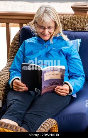 Ältere Frau, die ein Buch auf einer Terrasse im Freien liest Stockfoto