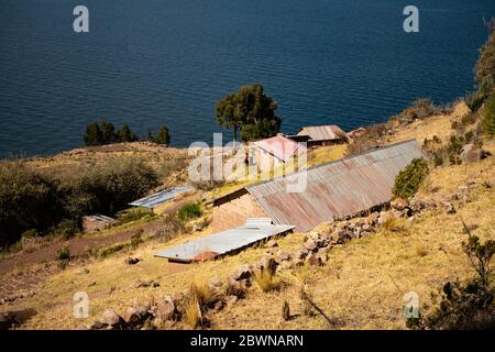 Der Blick auf eines der Häuser am Terrassenhang der Insel Taquile mit dem Titicacasee im Hintergrund. Stockfoto