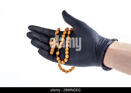 Hand in einem schwarzen medizinischen Schutzlatex Handschuh hält einen einfachen hölzernen christlichen Rosenkranz mit einem Kreuz isoliert auf weiß, ausgeschnitten. Sicheres Gebet Stockfoto