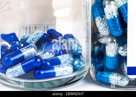Viele blau-weiße Pillen, transparente Tabletten mit Granulat in einem durchsichtigen Flaschenbehälter von der Seite gesehen, Makro, Nahaufnahme. Medikamente, Medikamente, Stockfoto