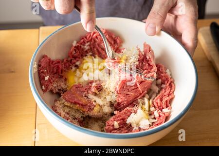 Hackfleisch und andere Zutaten mit einer Gabel in einer Schüssel mischen, Zubereitung zum Kochen von Fleischbällchen, ausgewählter Fokus, geringe Schärfentiefe, wenig Bewegung BL Stockfoto