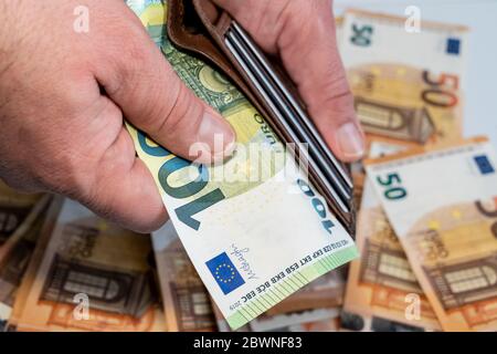 Hand eines Mannes, der eine braune Geldbörse mit einer 100-Euro-Banknote hält. Viele 50 Euro im Hintergrund. Hochwertige Fotos Stockfoto