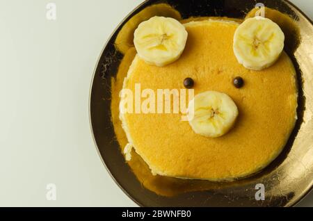 Kreative Mahlzeit für ein Kind, Pfannkuchen mit Banane und Schokolade in einem Gesicht kleine Bärenform, lustige Lebensmittel Stockfoto