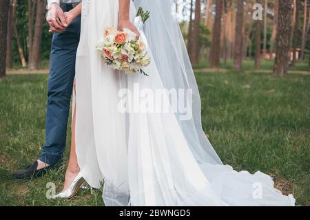 Eine Braut in einem schönen Kleid mit einem Zug hält einen Blumenstrauß und Grün Stockfoto