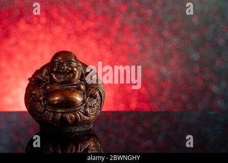 Chinesisch lachender buddha Hotei oder Budai auf einem rot-schwarzen Hintergrund mit Sternen und Spiegelung Stockfoto