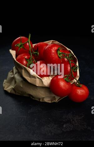 Frische reife rote Tomaten in Papiertüte auf dunklem Hintergrund. Einkaufskonzept für Lebensmittel Stockfoto