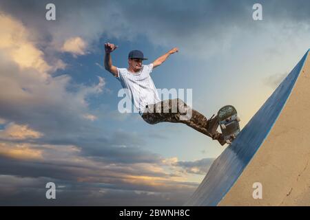 Der junge Skateboarder fährt sein Skateboard im Abendlicht am Rand einer Rampe entlang Stockfoto