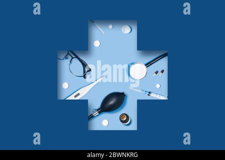3D Papier schneiden. Medizinische klassische blaue Hintergrund mit Spritze, Tabletten, Thermometer, Stethoskop, Gläser liegen in einem geschnitzten medizinischen Kreuz. Stockfoto