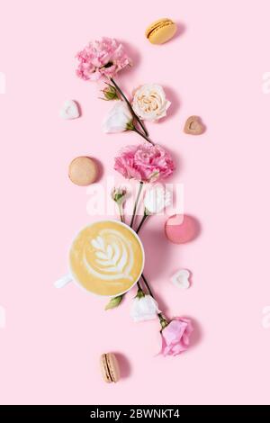 Köstlicher Cappuccino in Blumen und Makronen auf rosa Hintergrund. Positive Emotionen am Morgen. Stockfoto