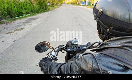 Motorradfahrer mit Helm. Biker-First-Person-Ansicht auf einem Motorrad Fahrten auf der Straße im Dorf, Blick auf die Straße Stockfoto