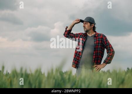 Verantwortungsvoller Weizenbauer Agrarwissenschaftler, der sich sein kultiviertes Getreideanbaugebiet ansieht, männlicher Farmarbeiter, der sich auf Ackerland posiert Stockfoto