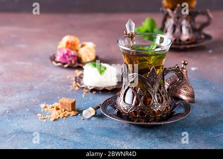 Traditioneller türkischer Tee mit Minzblättern und Süßigkeiten in einem traditionellen Glas auf betontem Hintergrund Stockfoto