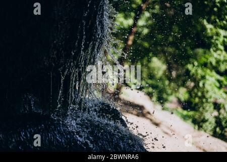 Wasser spritzt auf einen großen Stein. Spritzer eines kleinen Wasserfalls in der Grotte. Park mit einem natürlichen Wasserfall Stockfoto