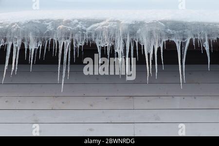 Gebäude mit Eiszapfen bedeckt, Nahaufnahme. Eis Stalaktit hängt vom Dach, Kopie Raum. Schlechte Wärmedämmung des Daches führt zur Bildung von ic Stockfoto