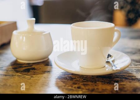 Aromatischer frischer Kaffee in einer weißen Tasse. Espresso in einer kleinen weißen Tasse und eine Zuckerdose in einem Sommercafé. Duftender frischer Kaffee in einem Restaurant Stockfoto