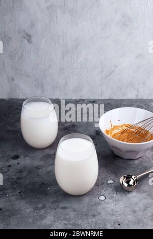 Beliebte Getränk koreanischen Dalgon Kaffee. Langer Löffel fügen Sie üppigen Schlagschaum auf Glas Milch auf grauem Hintergrund Stockfoto