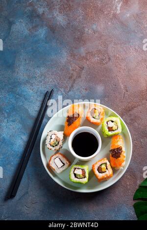 Verschiedene frische und leckere Sushi-Set auf Keramikplatte mit Schieferstöcken, Sauce auf Steingrund, flaches Lay Stockfoto