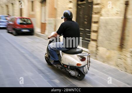 Mann auf einem weißen Roller auf den Straßen von Syrakus in Sizilien. Italien Stockfoto