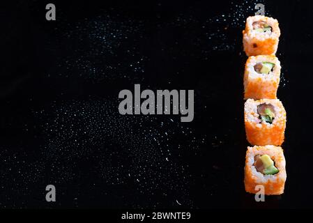 California Maki Sushi with Masago - Rolle aus Krabbenfleisch, Avocado, Gurke auf schwarzem Glasgrund, Kopierraum Stockfoto
