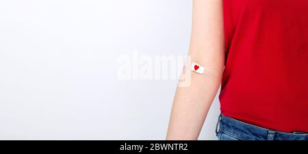 Blutspenderin. Junges Mädchen in rotem T-Shirt handtaped mit Patch mit rotem Herz nach dem Geben Blut auf grauem Hintergrund. Kopierbereich Stockfoto