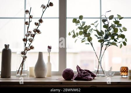 Vor dem Hintergrund des Fensters auf der Fensterbank befinden sich Vasen mit Blumen, vor dem Hintergrund von Blumen ein Strickprodukt mit Stricken Stockfoto