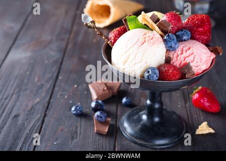 Trio aus leckeren Zitrone, Vanille und Erdbeere aromatisierten gefrorenen Dessert Eis in einer Metallschale mit Waffelstrohhalmen und Beeren auf Holz Stockfoto