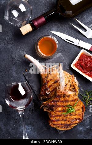 Saftiges gegrilltes Tomahawk-Rindssteak auf dem Knochen mit Rotwein, Gewürzen, frischem Rosmarin und Tomatensoße auf schwarzem Hintergrund, Draufsicht Stockfoto