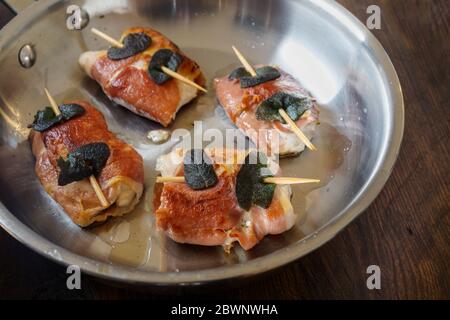 Gebratenes Hähnchen Saltimbocca mit Schinken und Salbeiblättern in einer Edelstahlpfanne auf rustikalem Holz, ausgewählter Fokus, schmale Schärfentiefe Stockfoto