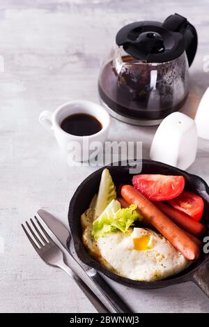 Englisches Frühstück in der Pfanne mit Spiegeleiern, Würstchen, Toast, Gemüse und Kaffee auf hellem Steingrund, flaches Lay Stockfoto