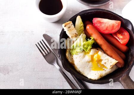 Englisches Frühstück in der Pfanne mit Spiegeleiern, Würstchen, Toast, Gemüse und Kaffee auf hellem Steingrund, flaches Lay Stockfoto